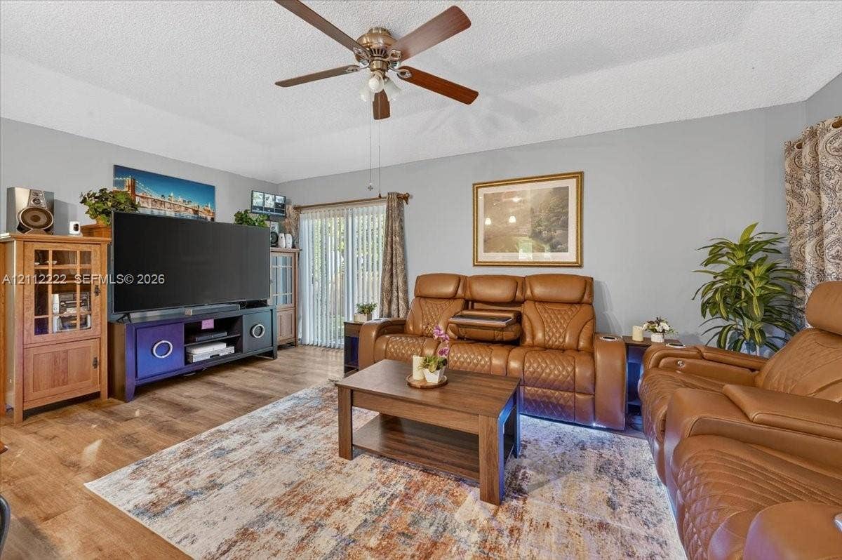 Living area featuring wood-finish flooring, a ceiling fan with integrated lighting, and sliding glass doors