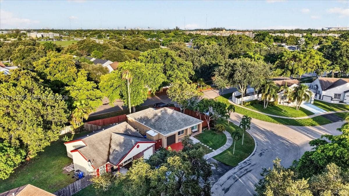 Aerial perspective of a single-story residence featuring a shingled roof, a paved driveway, a gated backyard, and mature surrounding landscape