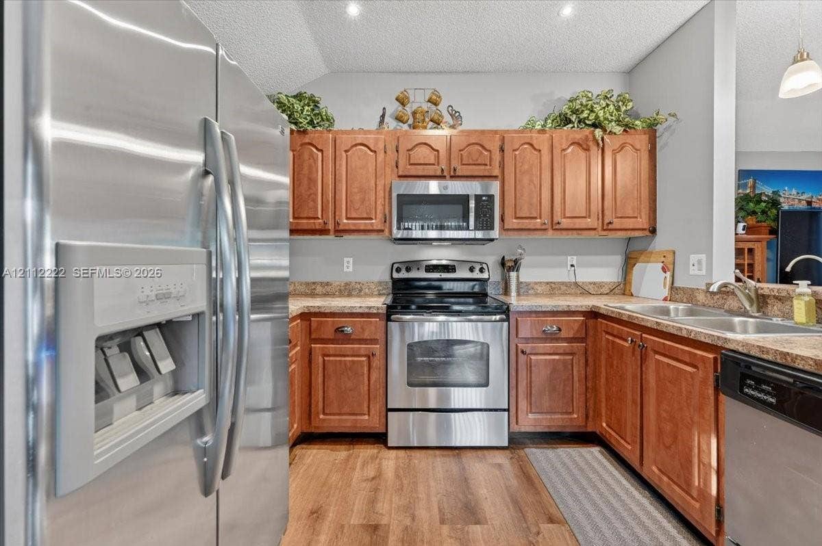 Kitchen featuring wood cabinetry, stainless steel appliances, neutral countertops, double-basin sink, and wood-finish flooring