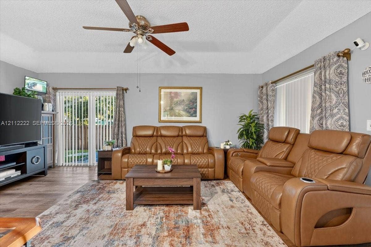 Living area featuring tray ceilings, wood-finish flooring, and sliding glass doors with vertical blinds