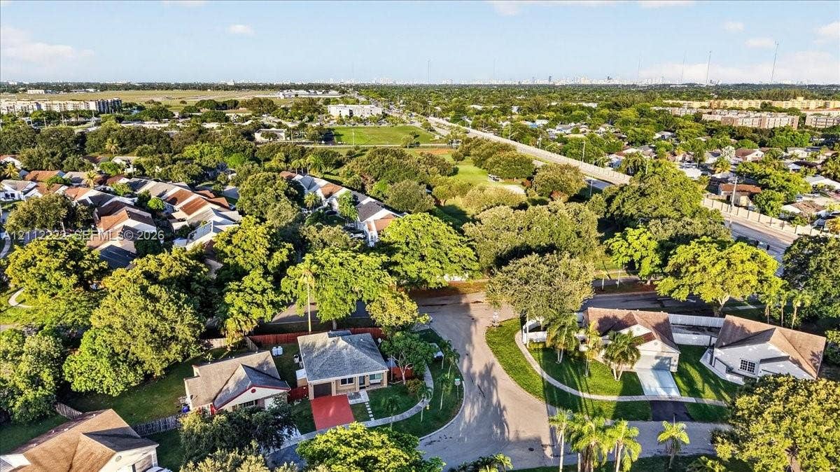Aerial perspective of a suburban neighborhood featuring mature trees, landscaped lawns, asphalt streets, and residential structures with shingle roofing