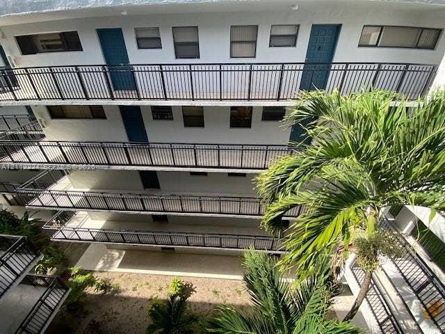 Multi-story building exterior featuring open-air walkways, black metal railings, and prominent palm landscaping