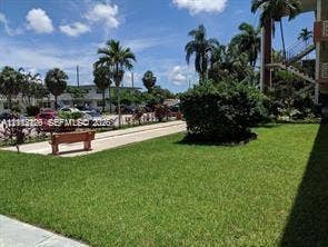 1450 NE 170th Street, #210, North Miami Beach, North Miami Beach, FL 33162 Common area grounds featuring manicured turf, mature palm trees, decorative shrubbery, and a paved walkway with a built-in bench