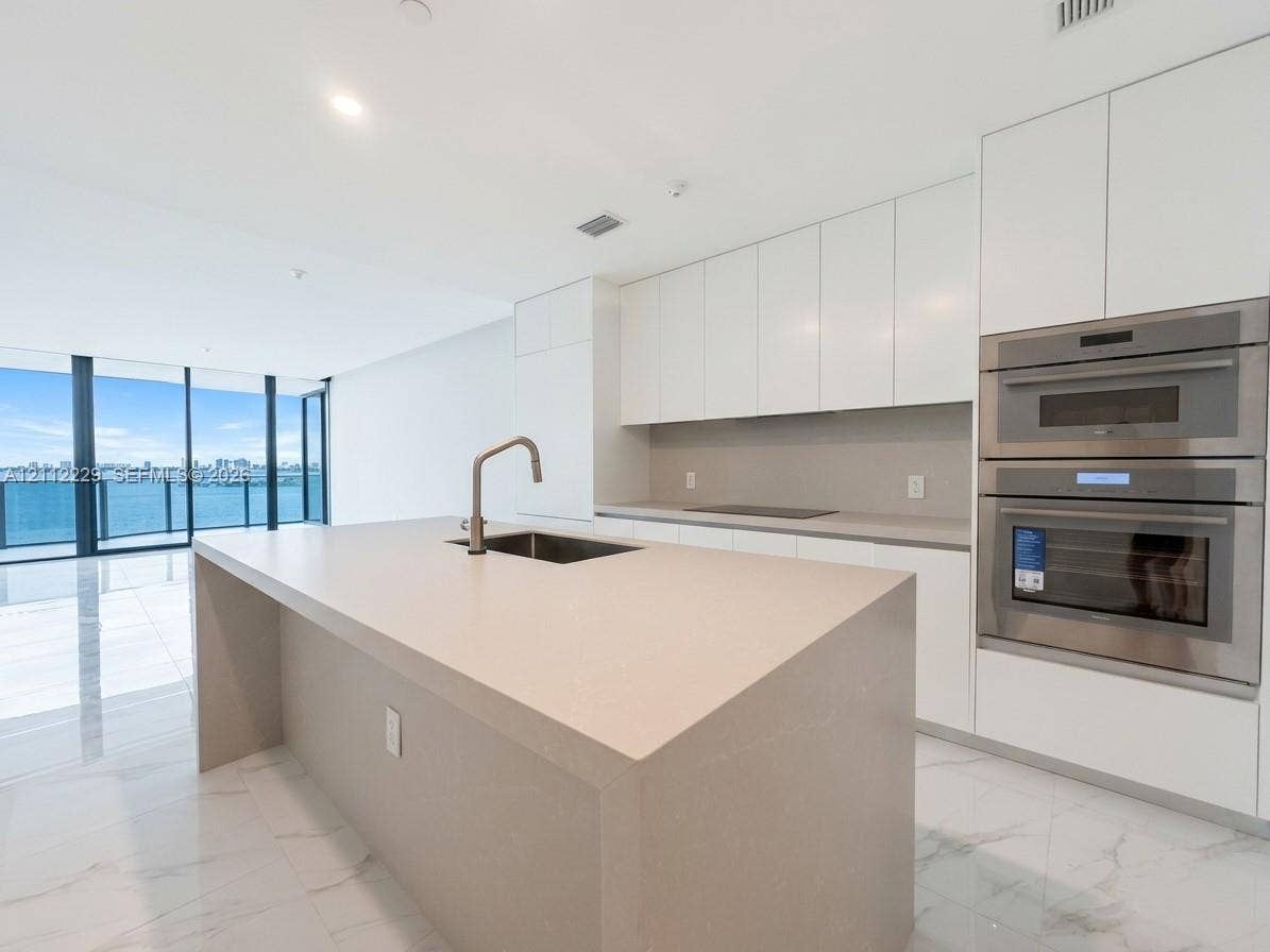 725 NE 24th Street, #706, Miami, Miami, FL 33137 Modern kitchen featuring white flat-panel cabinetry, a central island with a solid-surface countertop, stainless steel double wall ovens, and porcelain flooring throughout