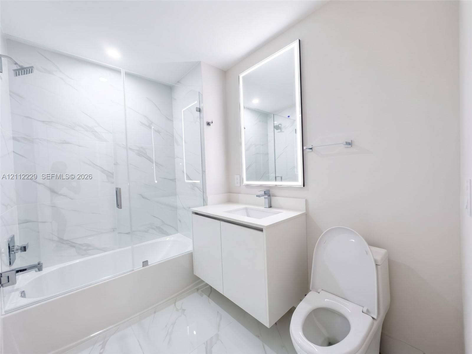725 NE 24th Street, #706, Miami, Miami, FL 33137 Bathroom featuring a glass-enclosed tub with floor-to-ceiling stone-style tile surround, floating vanity with a solid-surface countertop, and an integrated LED-lighted mirror