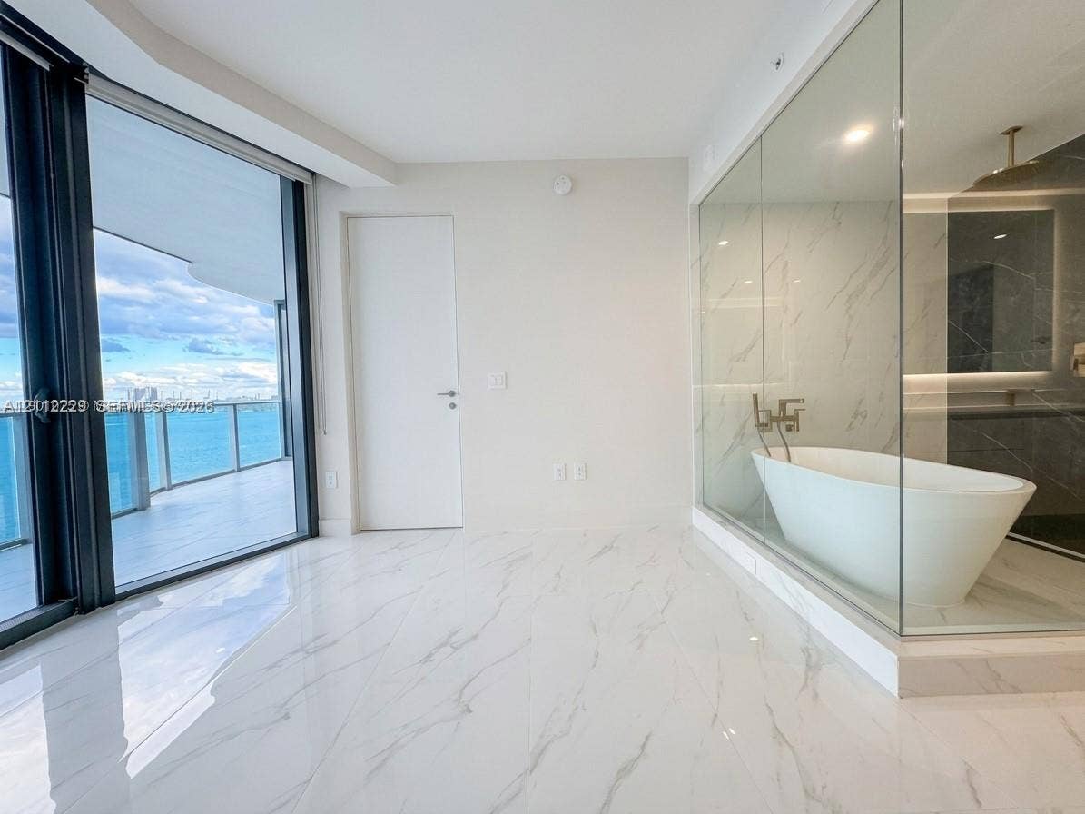 725 NE 24th Street, #706, Miami, Miami, FL 33137 Floor-to-ceiling glass balcony doors, polished stone-finish flooring, glass-enclosed bathroom partition, freestanding soaking tub, and wall-mounted plumbing fixtures