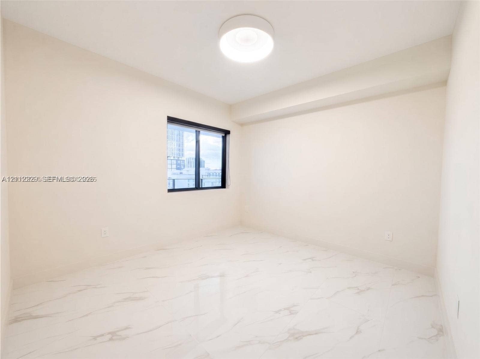 725 NE 24th Street, #706, Miami, Miami, FL 33137 Neutral-toned interior featuring stone-finish tile flooring, recessed window casing with dark framing, and a central circular flush-mount ceiling light fixture