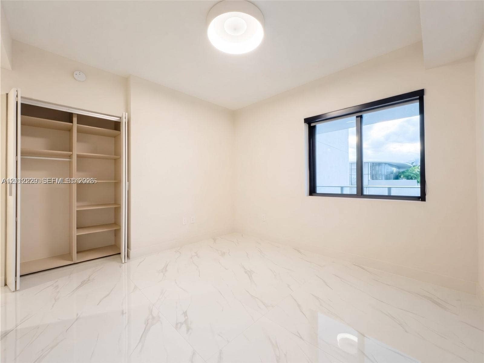 725 NE 24th Street, #706, Miami, Miami, FL 33137 Interior space featuring polished stone-finish flooring, a built-in closet with integrated shelving, a modern flush-mount ceiling light, and a black-framed window