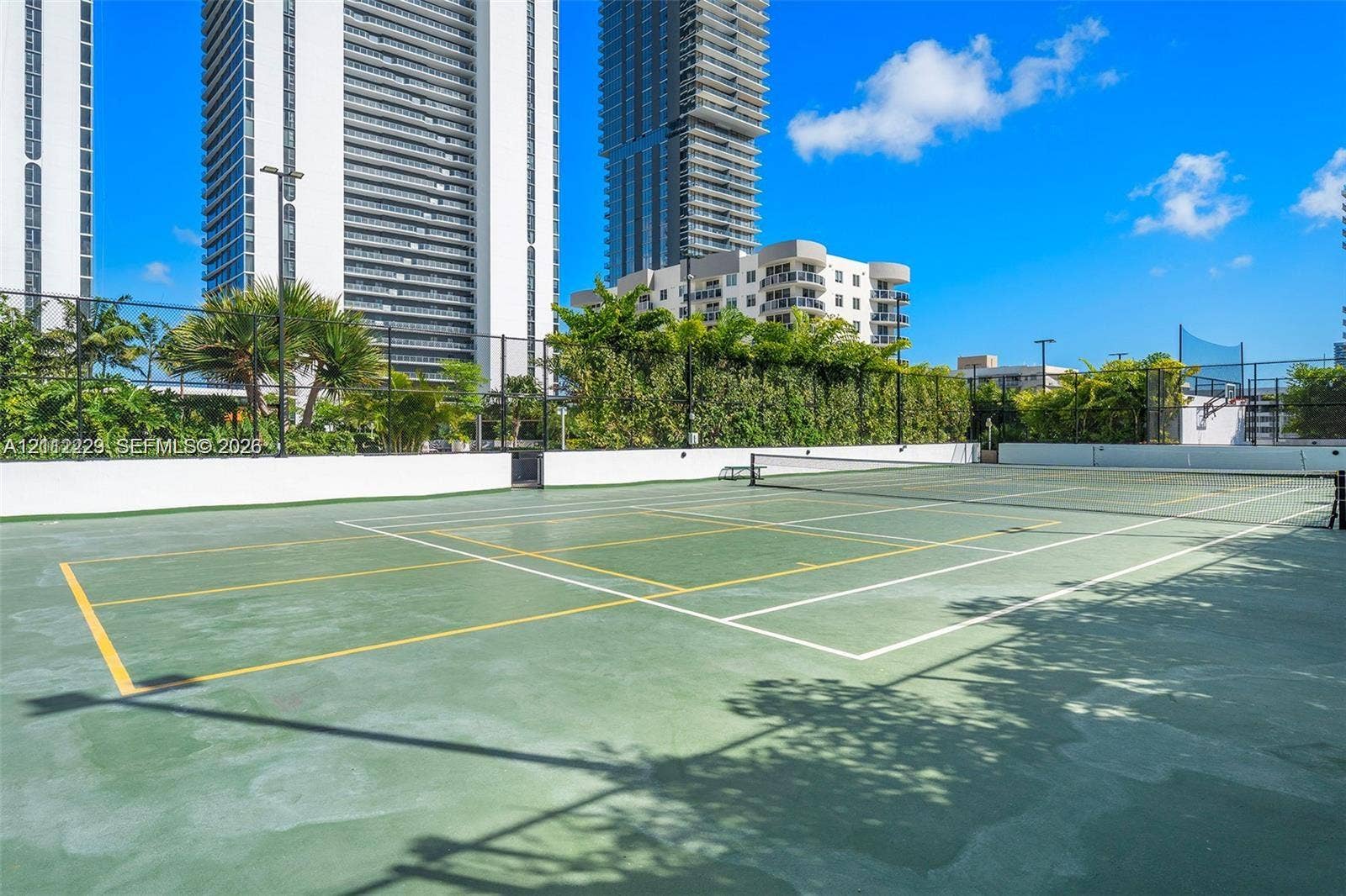 725 NE 24th Street, #706, Miami, Miami, FL 33137 Tennis court featuring a specialized green surface, perimeter fencing, and surrounding mature landscaping