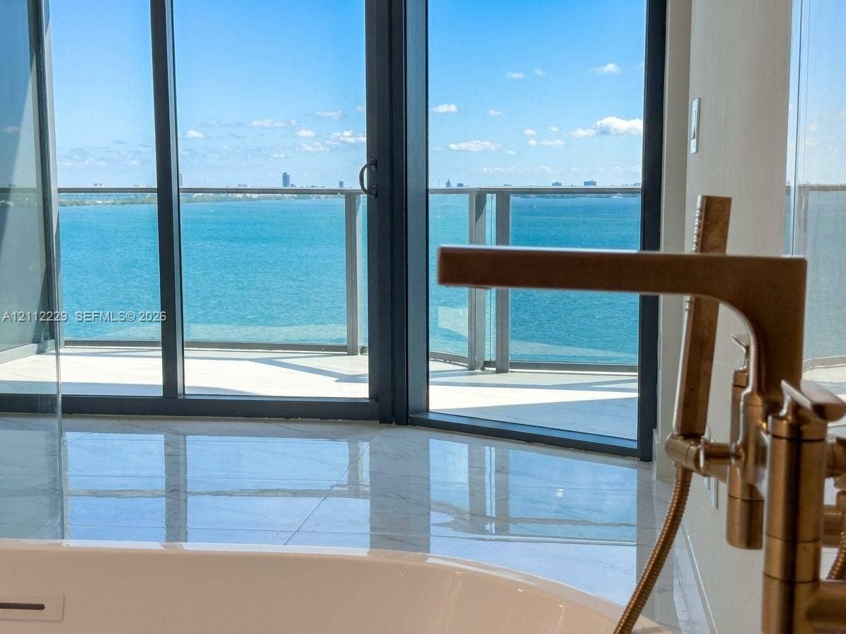 725 NE 24th Street, #706, Miami, Miami, FL 33137 Soaking tub with a metallic floor-mounted faucet, expansive floor-to-ceiling windows, and a private balcony featuring a glass railing