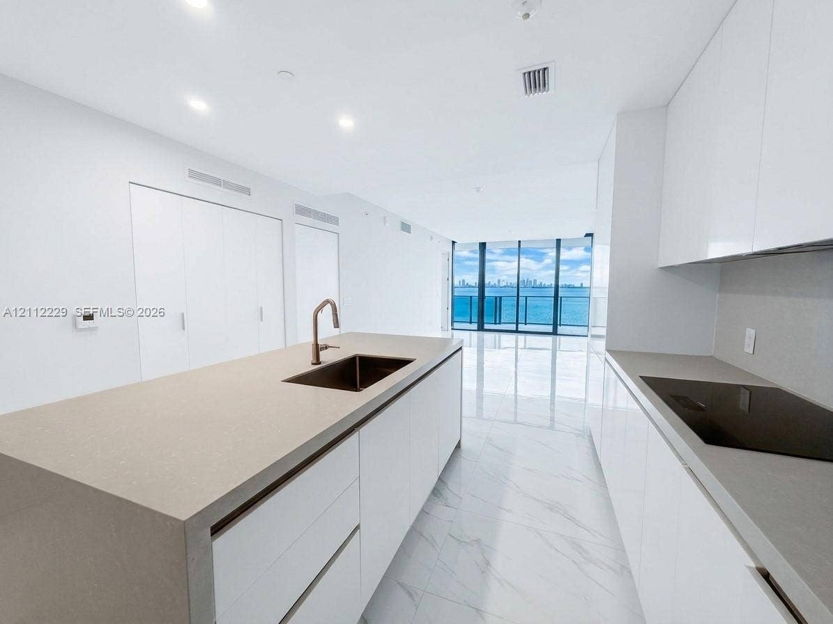 725 NE 24th Street, #706, Miami, Miami, FL 33137 Modern kitchen featuring a central island with a waterfall-edge countertop, gloss-finish cabinetry, an integrated cooktop, and floor-to-ceiling windows