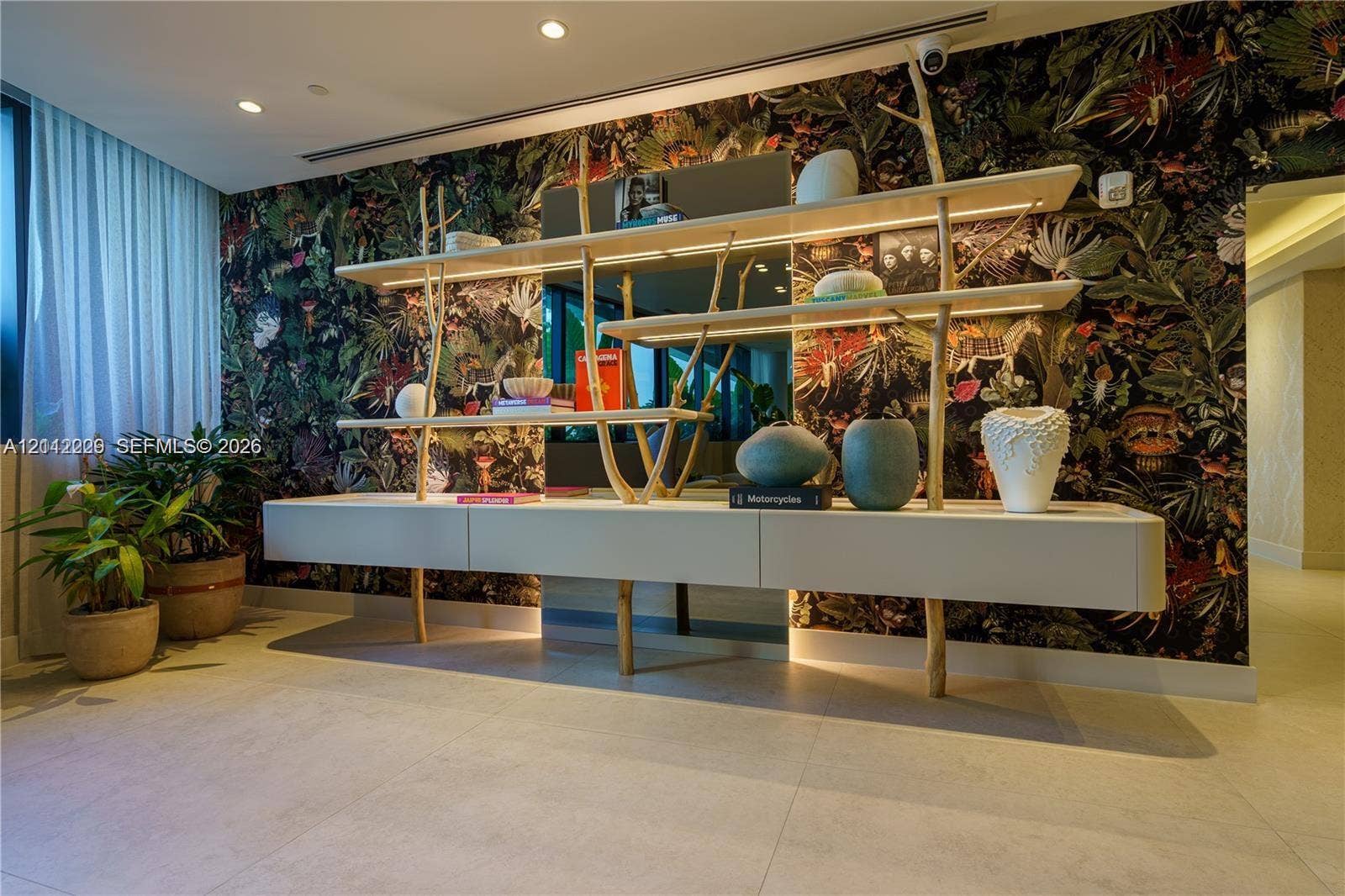 725 NE 24th Street, #706, Miami, Miami, FL 33137 Custom built-in wall unit featuring matte-finish cabinetry, integrated linear LED shelf lighting, and sculptural branch-style supports, set against a bold botanical-patterned accent wall with tile flooring