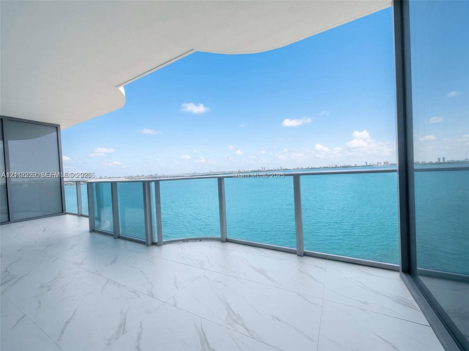 725 NE 24th Street, #706, Miami, Miami, FL 33137 Expansive private balcony featuring large-format stone-patterned tile flooring, a curved architectural overhang, floor-to-ceiling glass panel railings, and full-height sliding glass doors