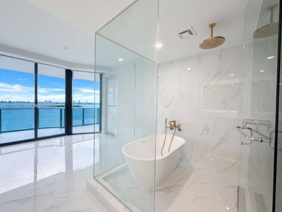 725 NE 24th Street, #706, Miami, Miami, FL 33137 Floor-to-ceiling glass wall, freestanding soaking tub, rainfall shower head, stone-finish tile wall and flooring, and gold-tone fixtures