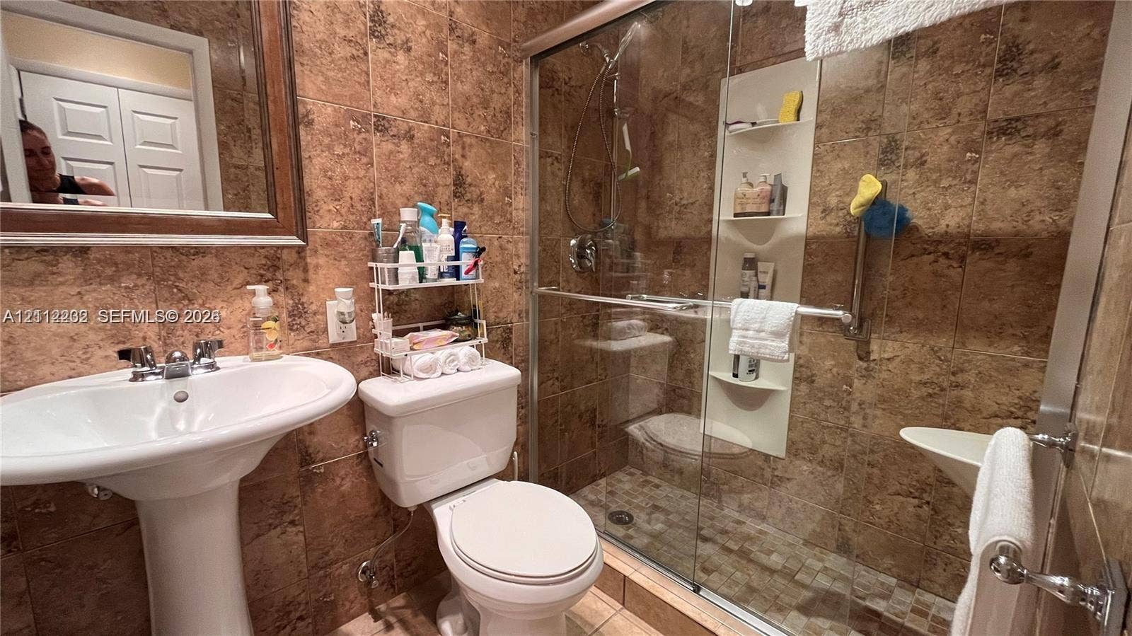2001 S Ocean Drive, #55, Hallandale Beach, Hallandale Beach, FL 33009 Bathroom featuring floor-to-ceiling stone wall tiling, a white pedestal sink with metallic fixtures, and a glass-enclosed shower with a built-in recessed shelf