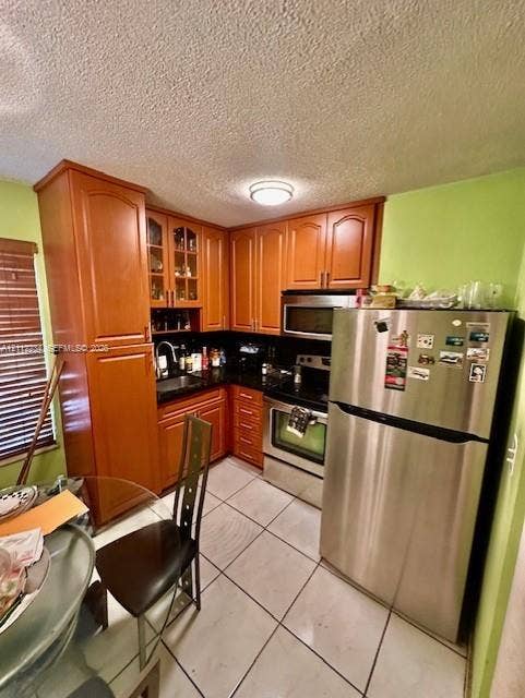 820 Salzedo Street, #305, Coral Gables, FL 33134 Kitchen featuring wood cabinetry with glass-panel upper doors, dark stone-finish countertops, stainless steel appliances, ceramic tile flooring, and a flush-mount ceiling light