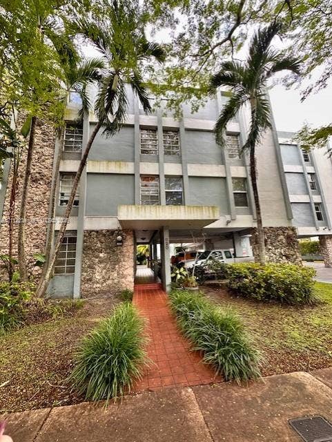 820 Salzedo Street, #305, Coral Gables, FL 33134 Multi-story facade featuring natural stone masonry, a covered entryway, and a brick-paved walkway surrounded by mature landscaping and palm trees