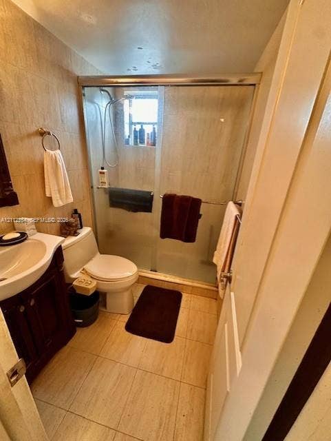 820 Salzedo Street, #305, Coral Gables, FL 33134 Bathroom featuring neutral stone-finish wall and floor tiling, dark wood cabinetry with a recessed sink, and a walk-in shower enclosure with a sliding glass door and integrated handheld showerhead