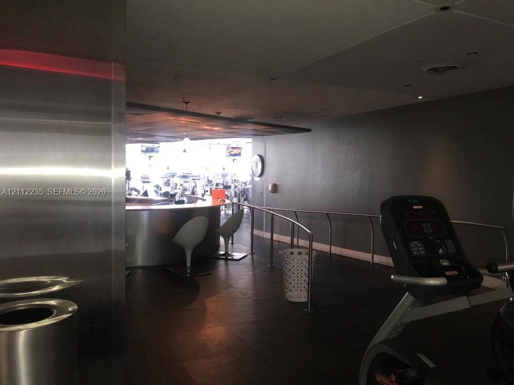 Fitness area featuring dark tile flooring, a curved stainless steel bar, recessed ceiling lighting, and metal handrails