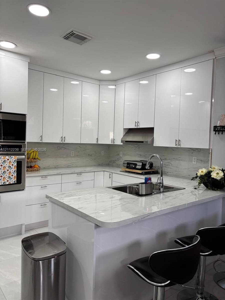 13946 SW 276th Street, #0, Homestead, FL 33032 Kitchen featuring high-gloss white cabinetry, stone-patterned countertops, integrated stainless steel double oven, stainless steel range hood, and a double-basin undermount sink
