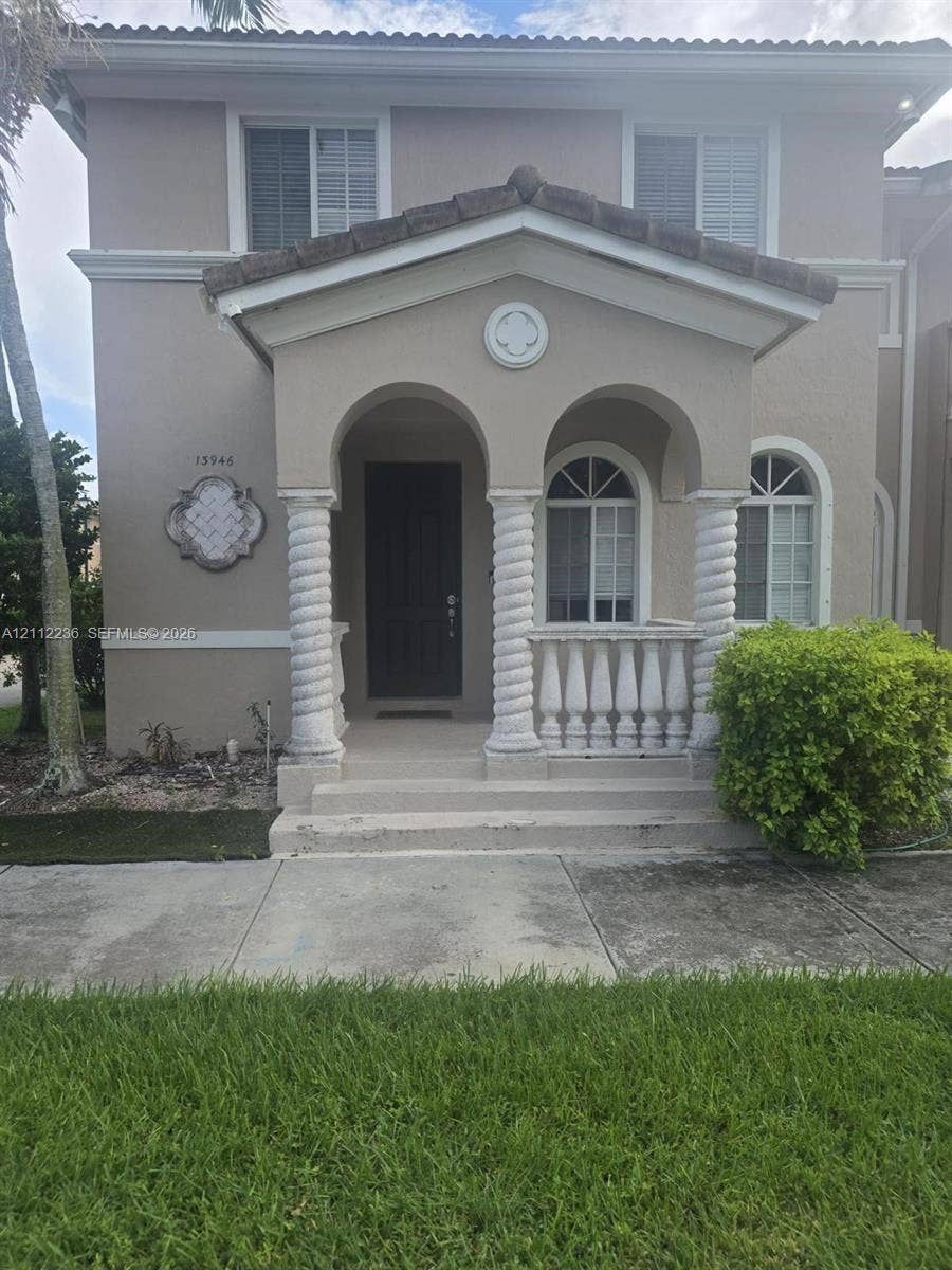 13946 SW 276th Street, #0, Homestead, FL 33032 Two-story exterior featuring a covered front porch with spiral columns, decorative stone balustrade, arched window casings, and a tiled gable roof