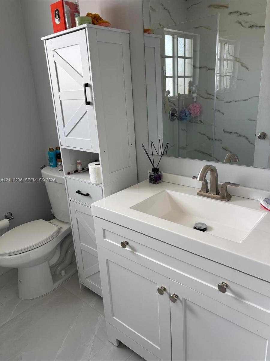 13946 SW 276th Street, #0, Homestead, FL 33032 Bathroom featuring a white vanity with an integrated basin, quartz-style countertop, tall built-in storage cabinetry with matte black hardware, and large-format tile flooring