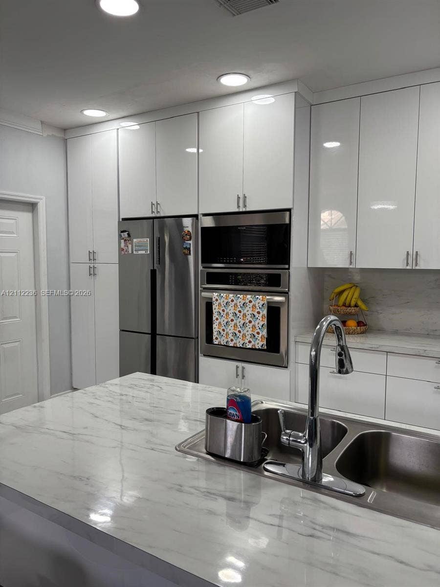 13946 SW 276th Street, #0, Homestead, FL 33032 Kitchen featuring high-gloss white cabinetry, stone-finish countertops, stainless steel appliances, built-in double wall ovens, and a double-basin undermount sink with a gooseneck faucet