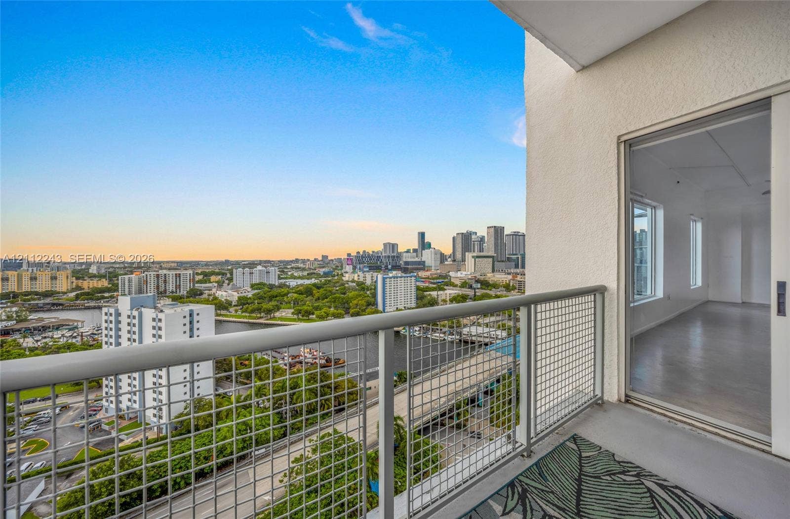 Private balcony with a metal wire railing and concrete flooring, featuring an expansive skyline and water backdrop