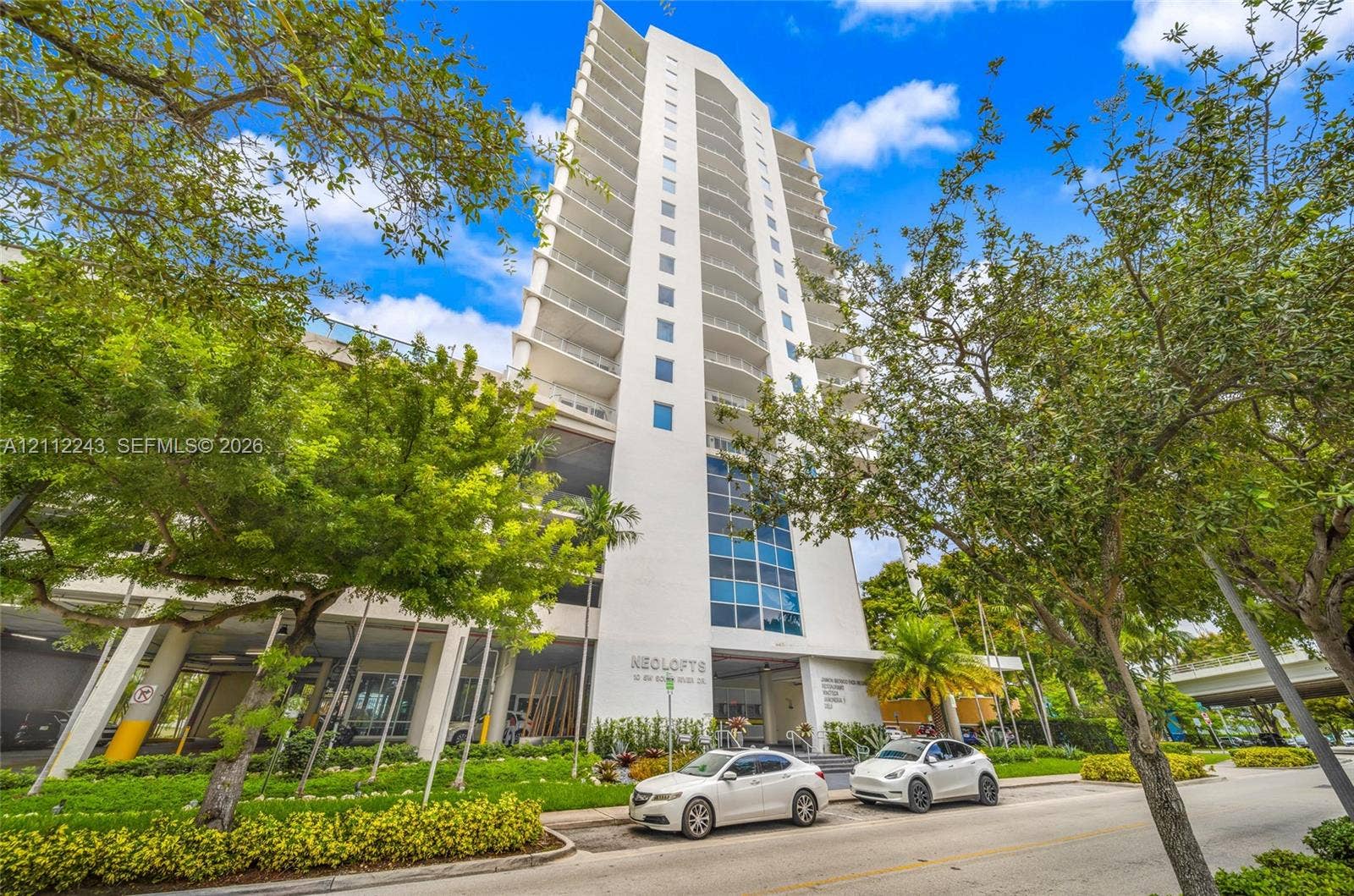 High-rise residential building featuring white stucco facade, tiered glass-railed balconies, and floor-to-ceiling blue-tinted windows