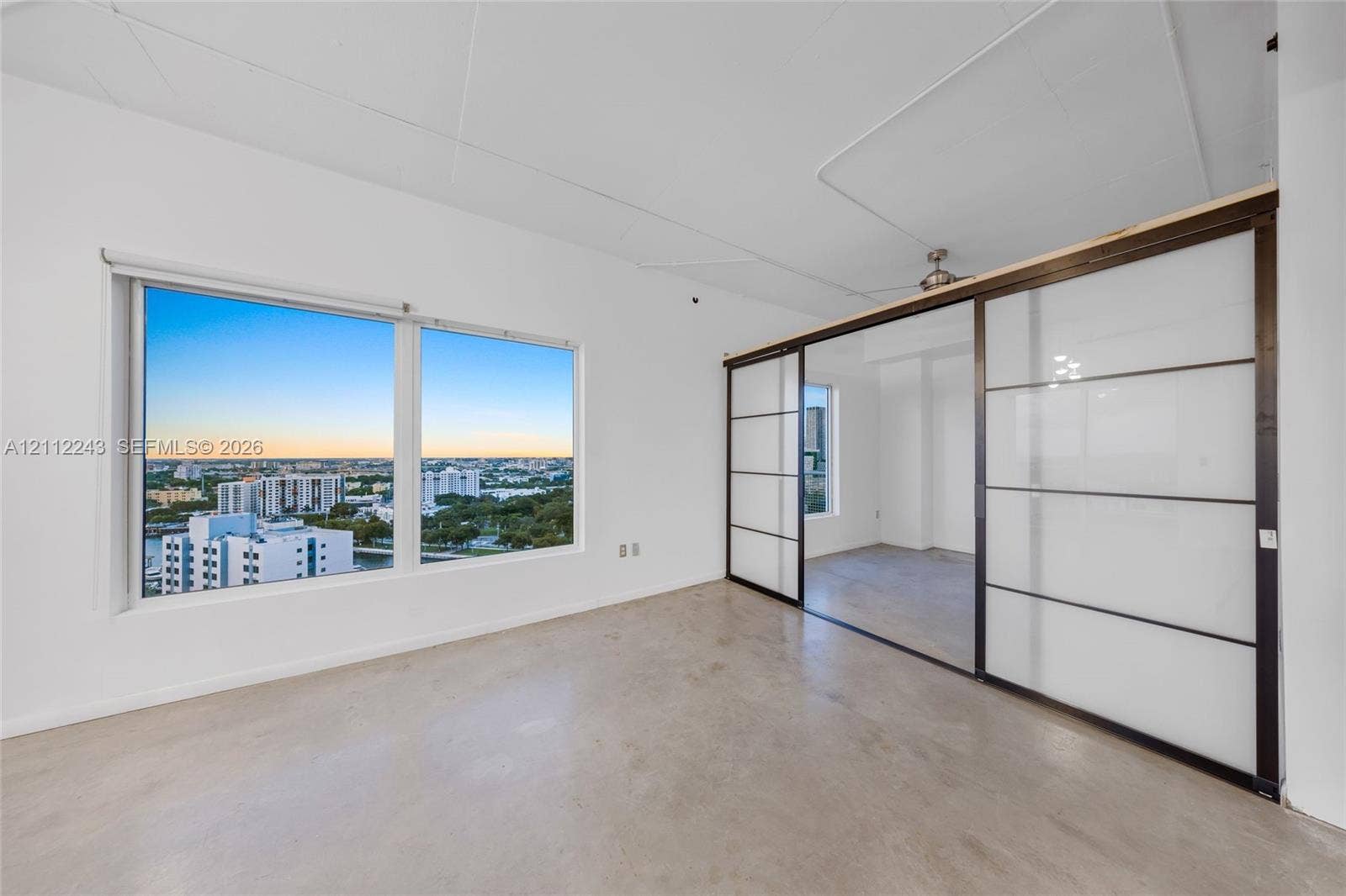 Polished concrete flooring, expansive windows with cityscape backdrop, and floor-to-ceiling sliding panels with opaque glass inserts