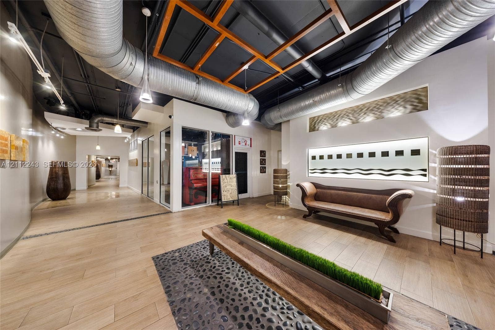 Industrial-style interior featuring an exposed high ceiling with metallic ductwork, grid-patterned wood framing, wood-finish tile flooring, and decorative pebble inlay accents