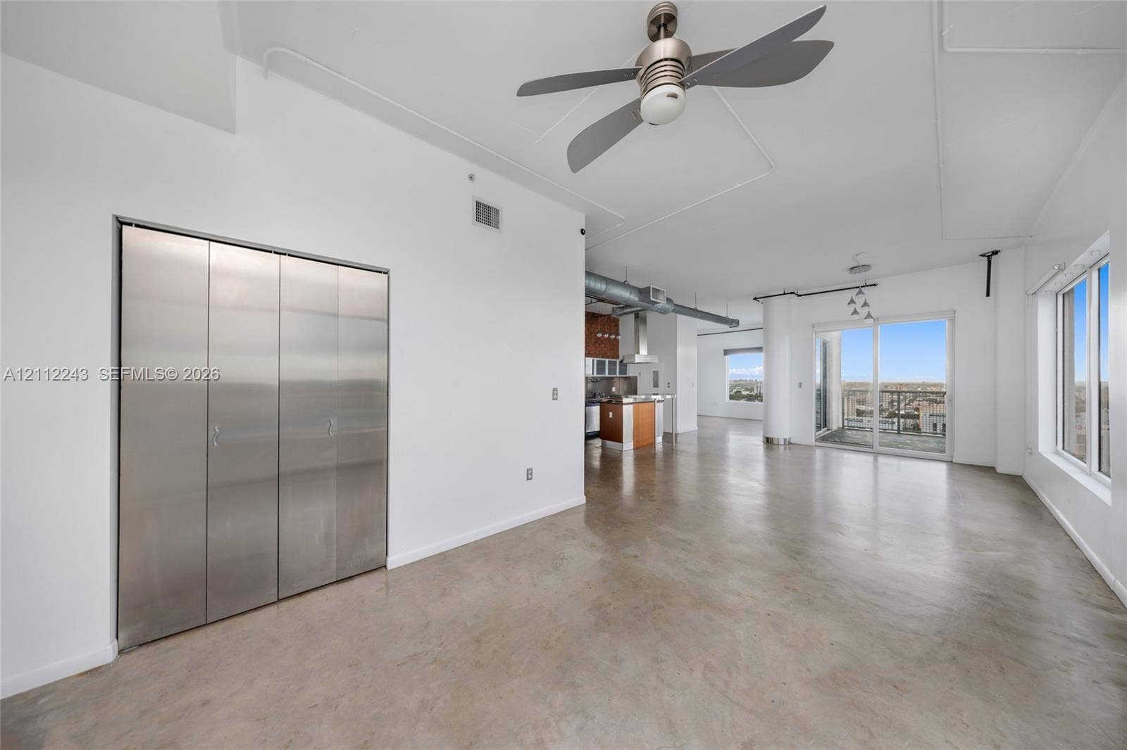 Polished concrete flooring, floor-to-ceiling metal-clad closet doors, industrial-style exposed ductwork, and sliding glass doors with exterior balcony access