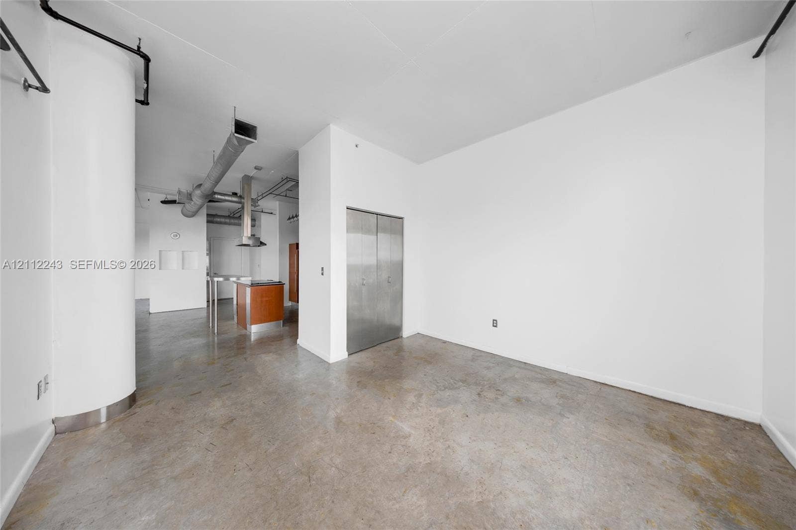Industrial-style interior featuring polished concrete flooring, exposed overhead ductwork, a curved architectural column, and stainless steel closet doors