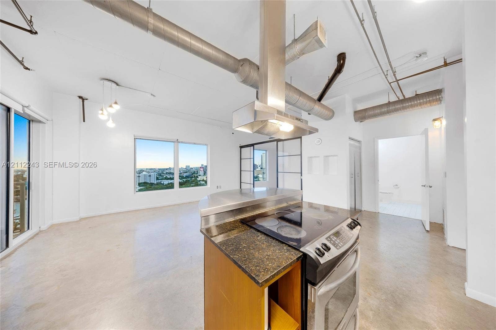 Industrial-style loft featuring exposed ductwork, concrete flooring, stone-surfaced kitchen island, stainless steel range hood, and floor-to-ceiling glass windows