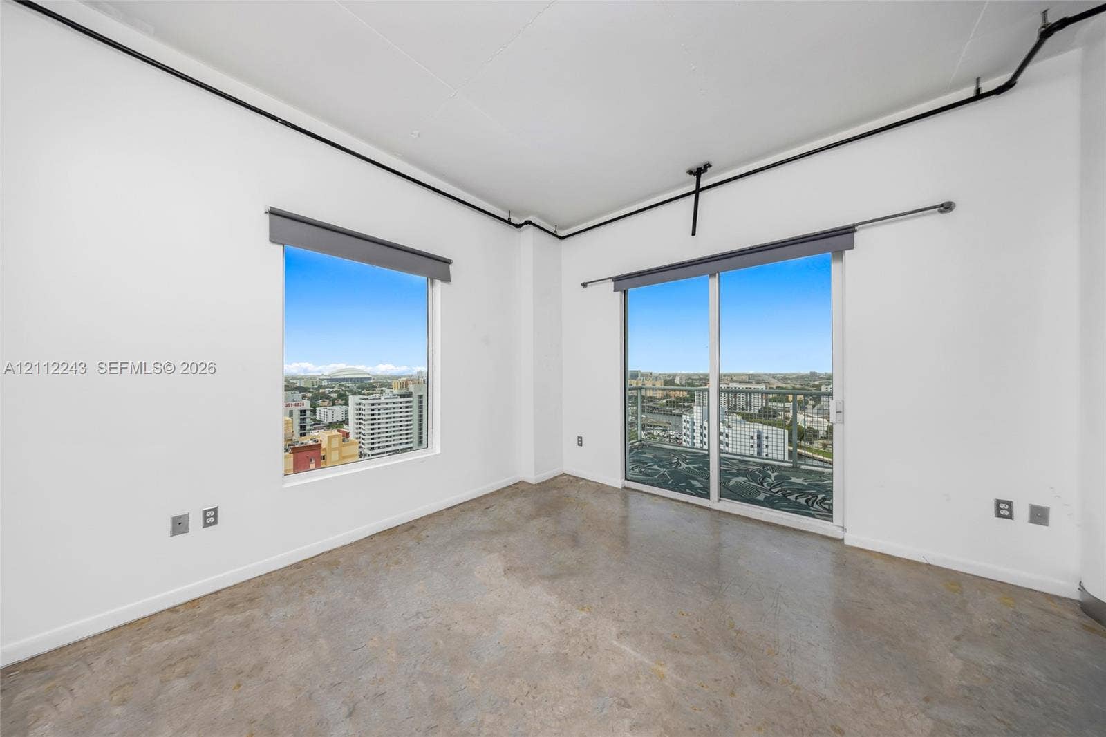 Polished concrete flooring, floor-to-ceiling window, glass sliding door, metal balcony railing, and exposed ceiling conduit