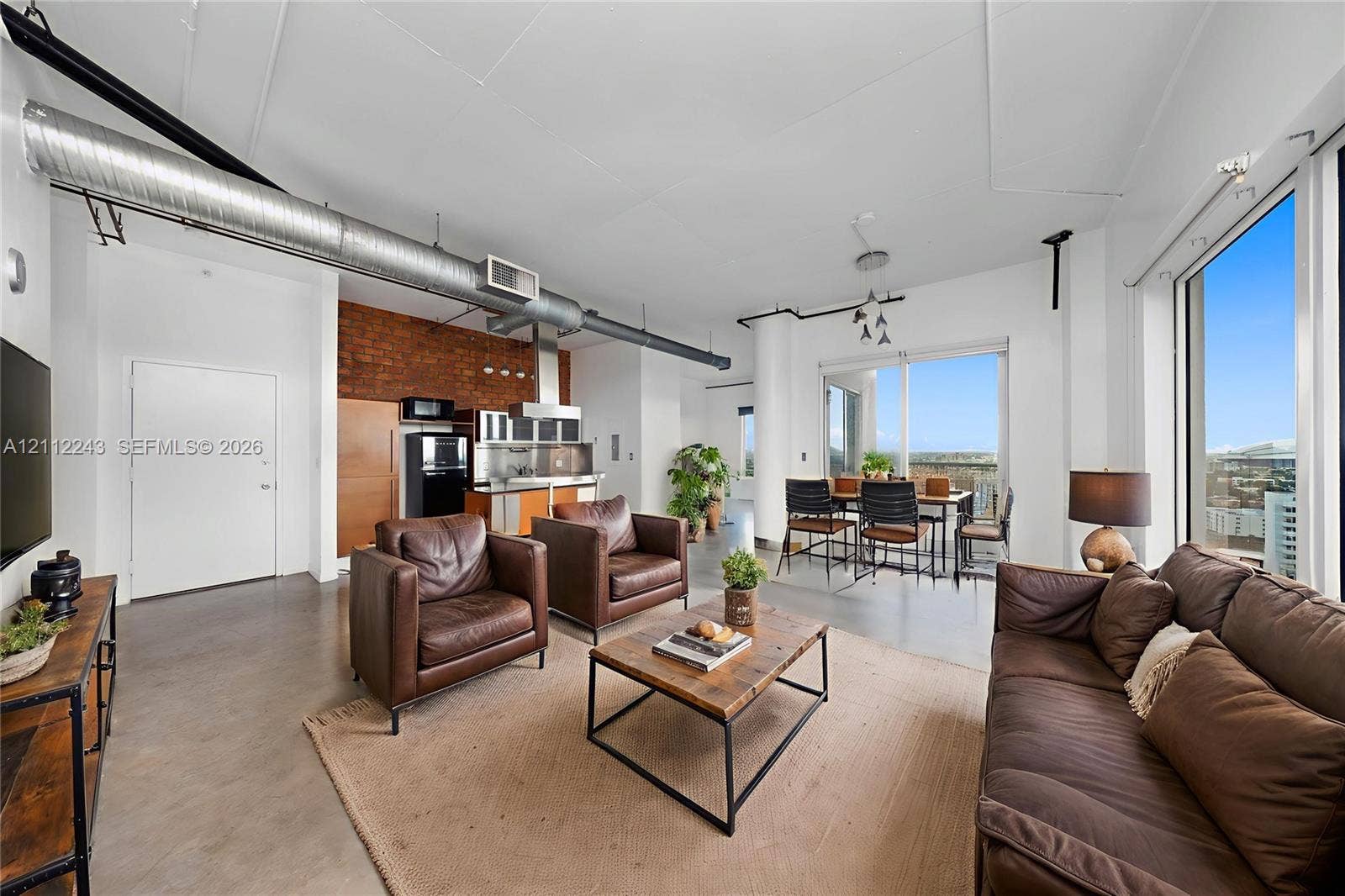 Industrial-style interior featuring exposed brick wall accents, polished concrete flooring, soaring ceilings with exposed mechanical ductwork, and floor-to-ceiling windows