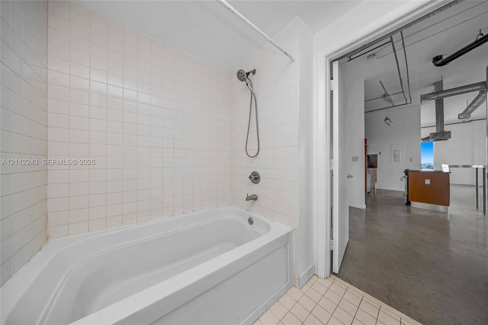 Bathroom featuring a white deep-basin soaking tub, wall-mounted handheld showerhead, ceramic tile surround, and neutral floor tiling
