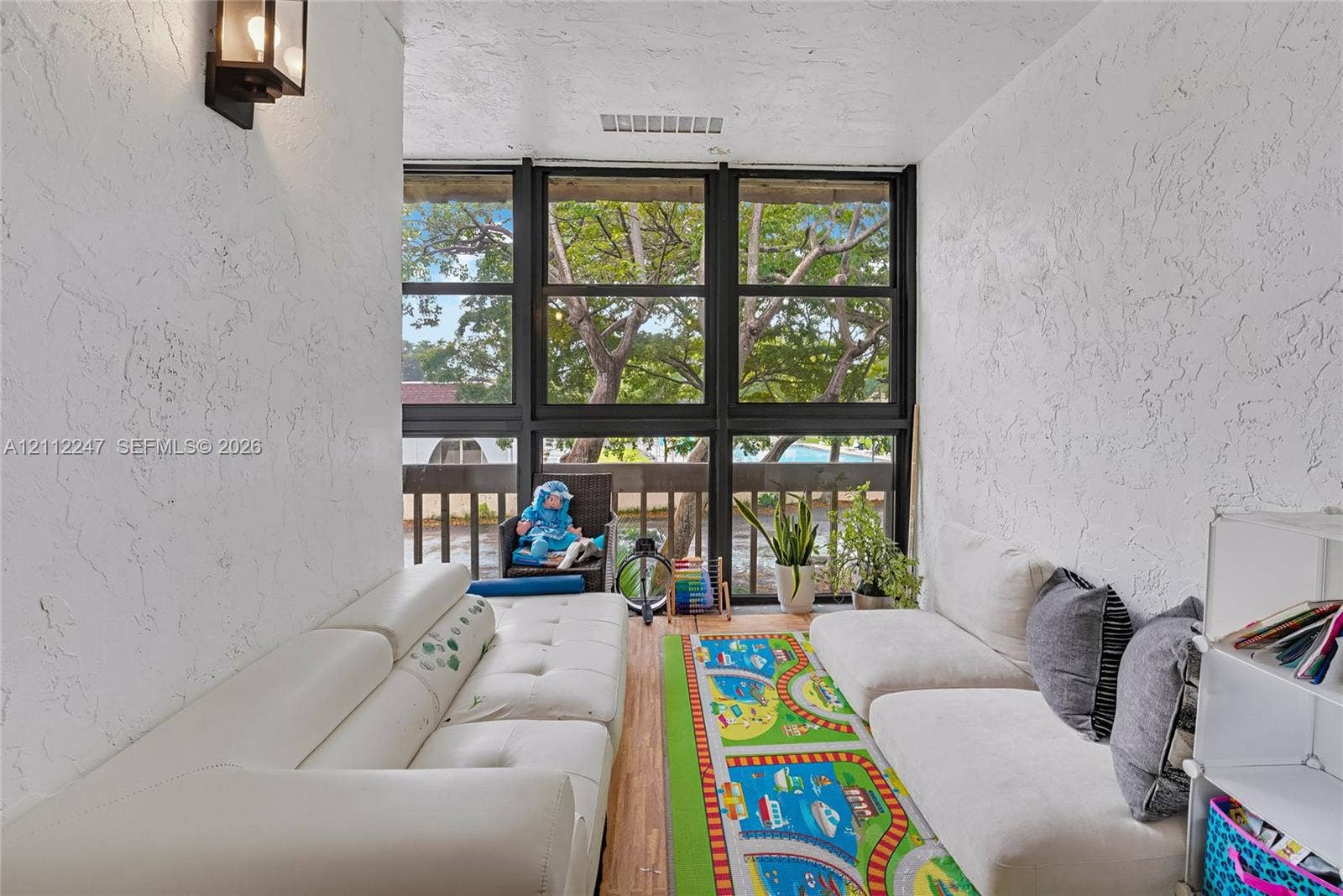 Enclosed sunroom featuring floor-to-ceiling windows, textured wall finish, and wood-finish flooring with a wall-mounted light fixture
