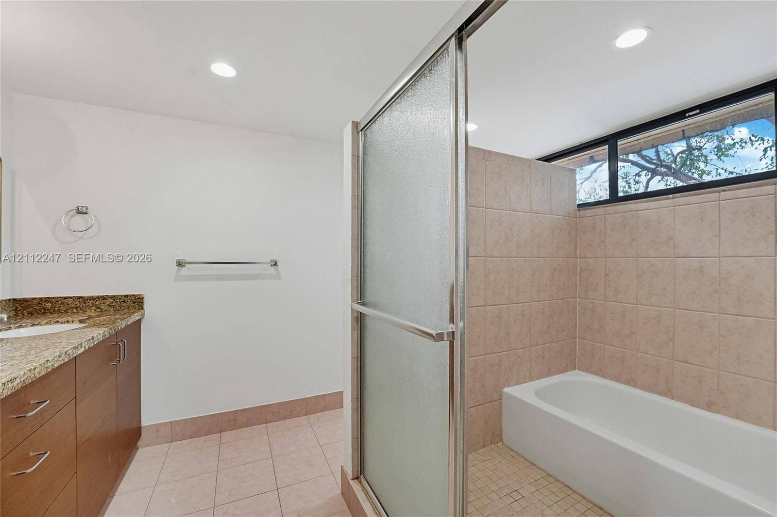 Bathroom featuring a vanity with stone-finish countertop, tiled shower-tub combination with sliding glass doors, horizontal clerestory window, and recessed ceiling lighting
