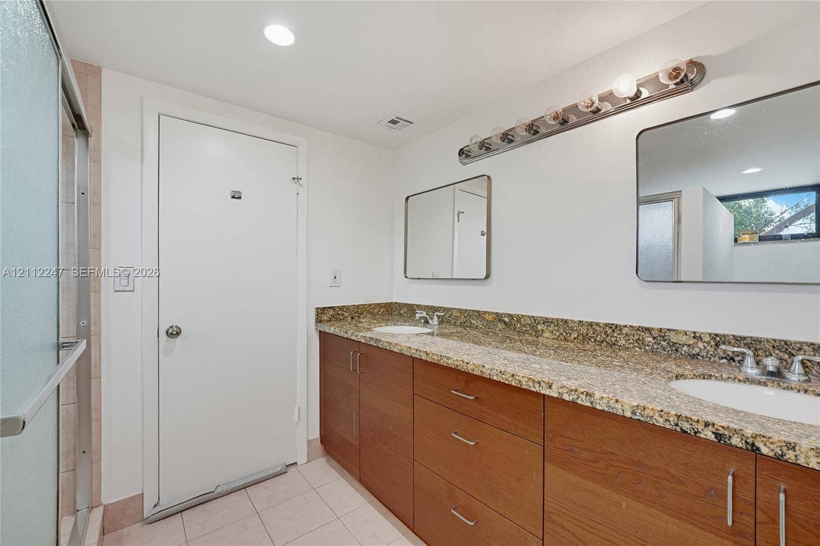 Dual-sink vanity with stone countertops, wooden cabinetry, two wall-mounted mirrors, and tiled flooring