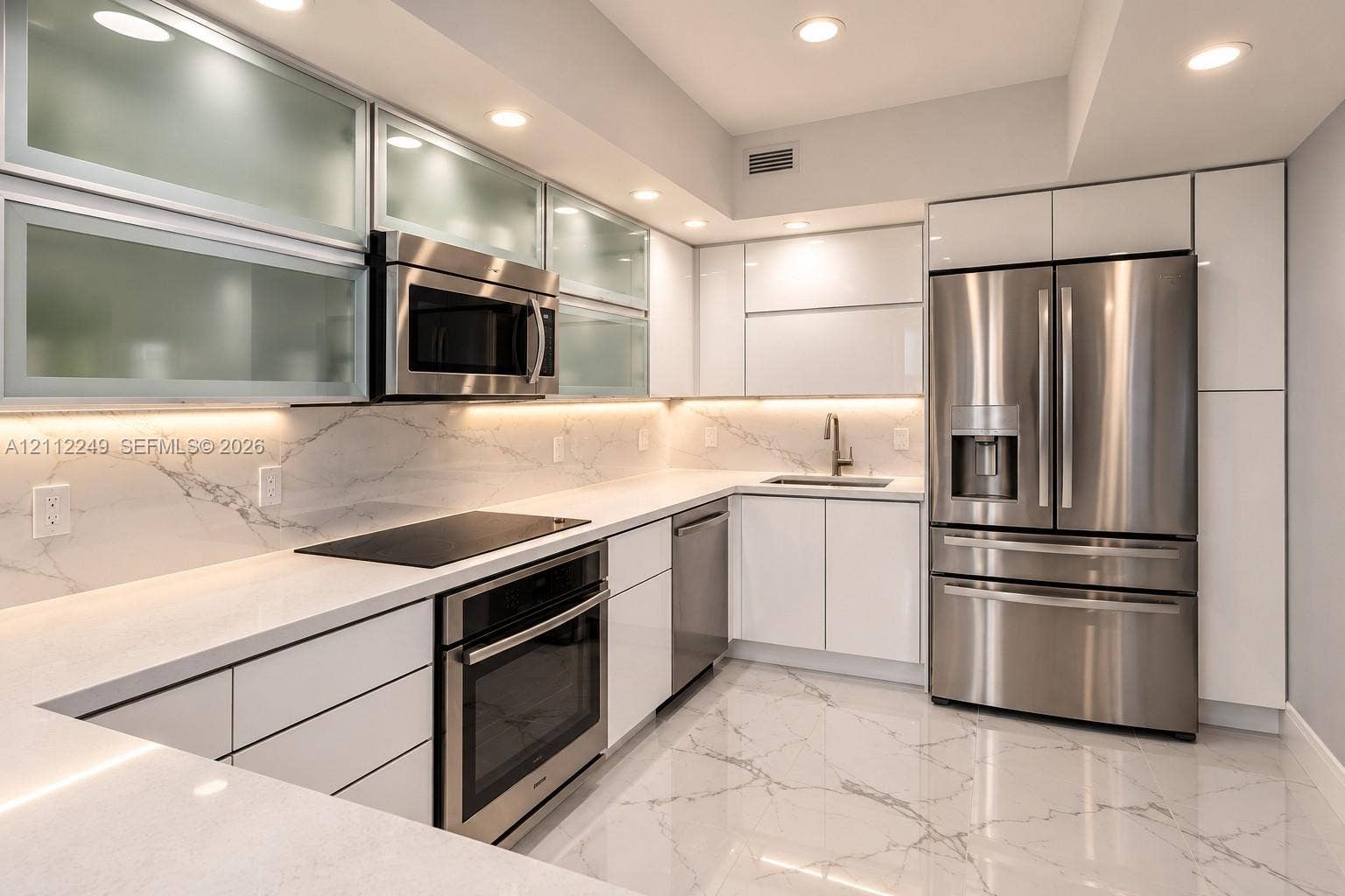 Modern kitchen featuring high-gloss cabinetry, upper glass-front display cabinets, stone-surfaced countertops, integrated under-cabinet lighting, and stainless steel appliances