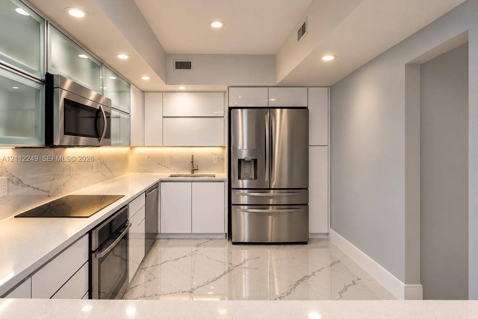 Contemporary kitchen featuring high-gloss cabinetry, stainless steel appliances, white stone-finish countertops with matching backsplash, and polished stone-finish flooring