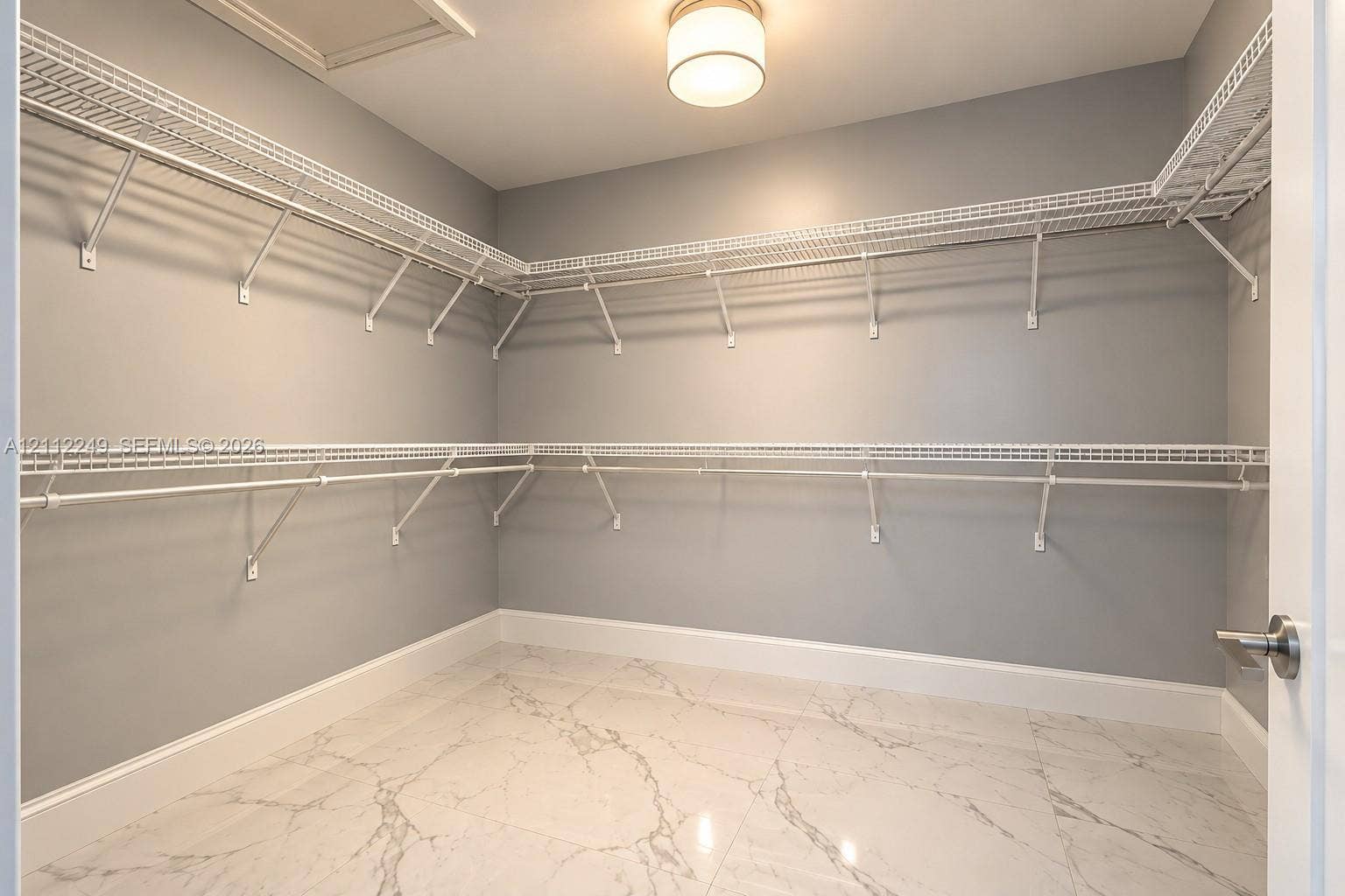 Walk-in closet featuring large-format tile flooring with a veined pattern, multi-tiered white wire shelving, and a flush-mount drum ceiling light fixture