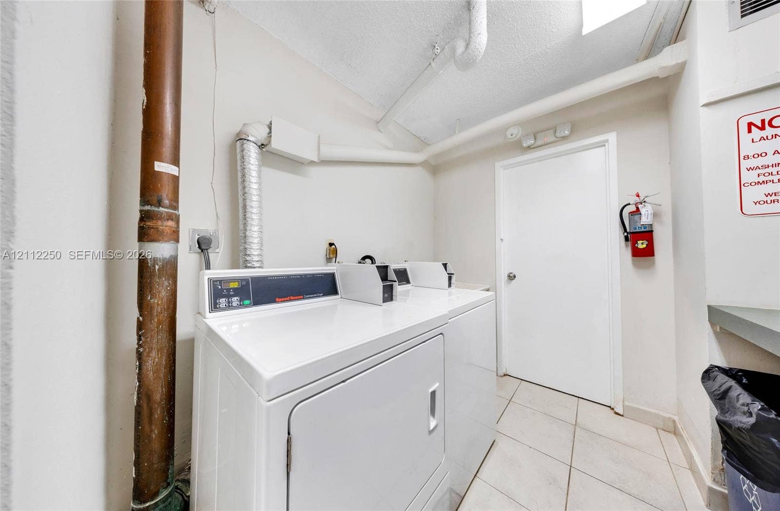 5838 Collins Avenue, #2F, Miami Beach, FL 33140 Laundry facility featuring coin-operated appliances, white tiled flooring, and a solid-core interior door