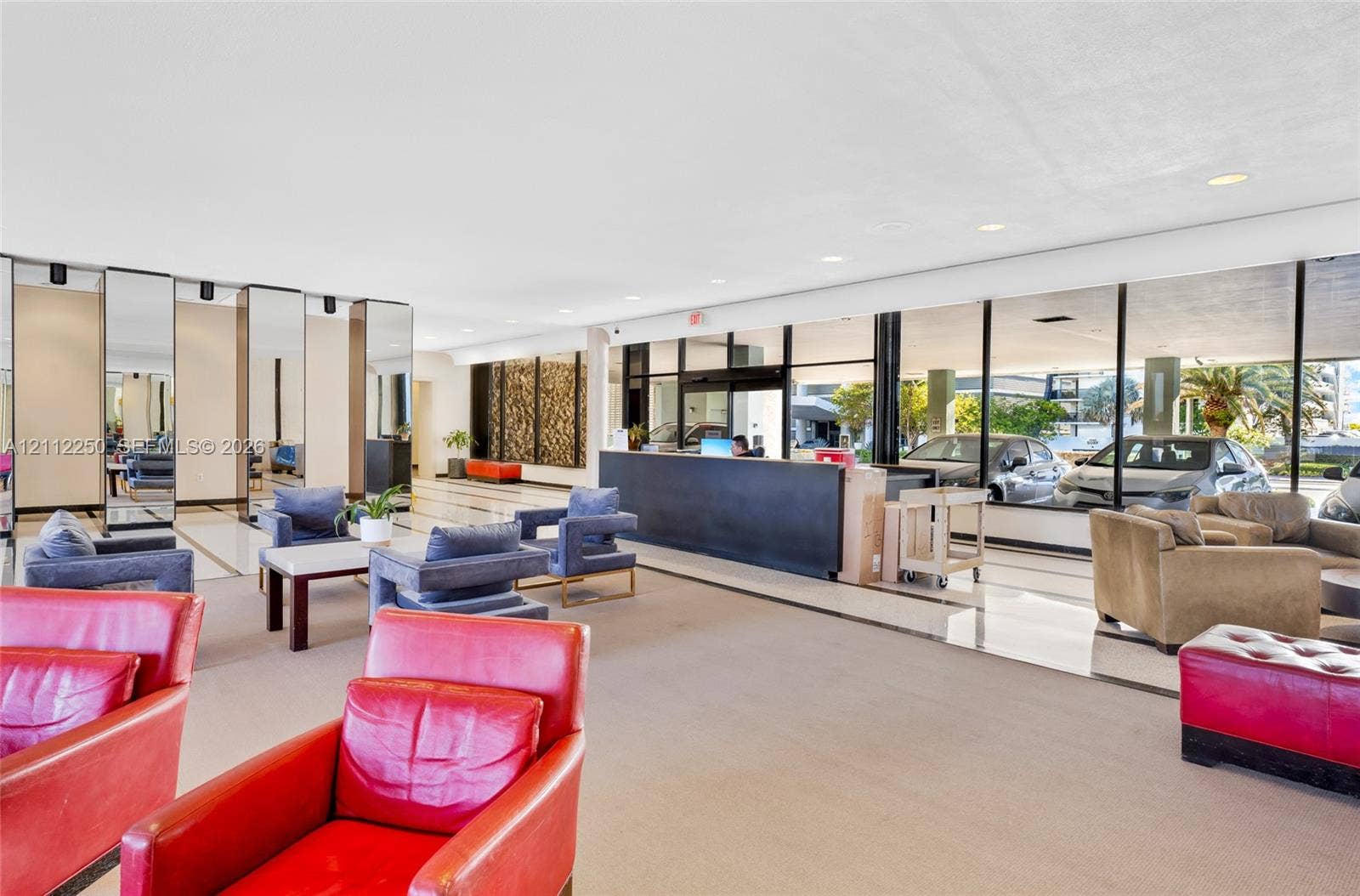 5838 Collins Avenue, #2F, Miami Beach, FL 33140 Expansive lobby featuring floor-to-ceiling glass paneling, full-height mirrored wall panels, polished stone flooring, and a built-in reception desk