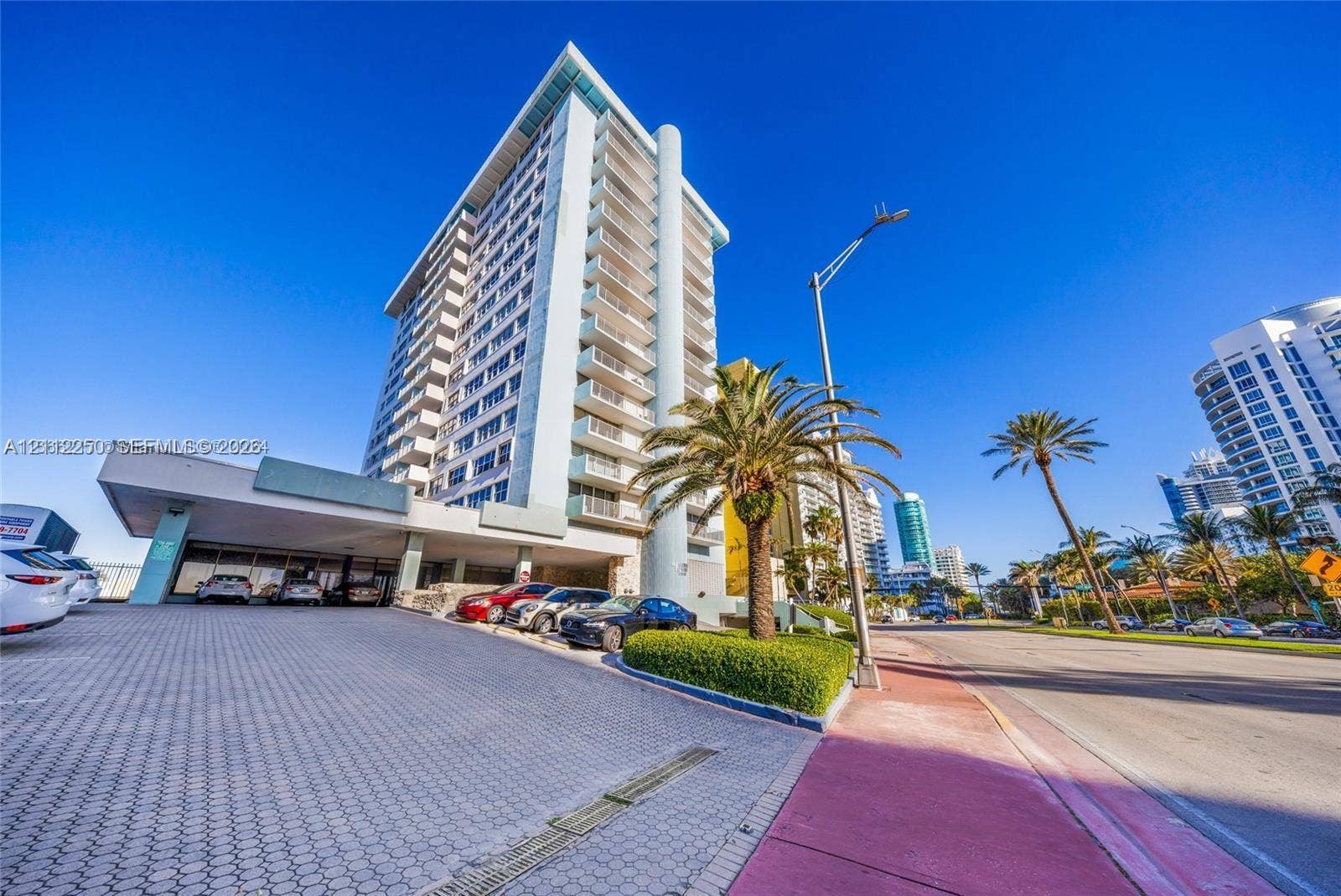 5838 Collins Avenue, #2F, Miami Beach, FL 33140 High-rise residential building featuring a covered portico entry, paved driveway, multi-level balconies, and exterior landscape plantings