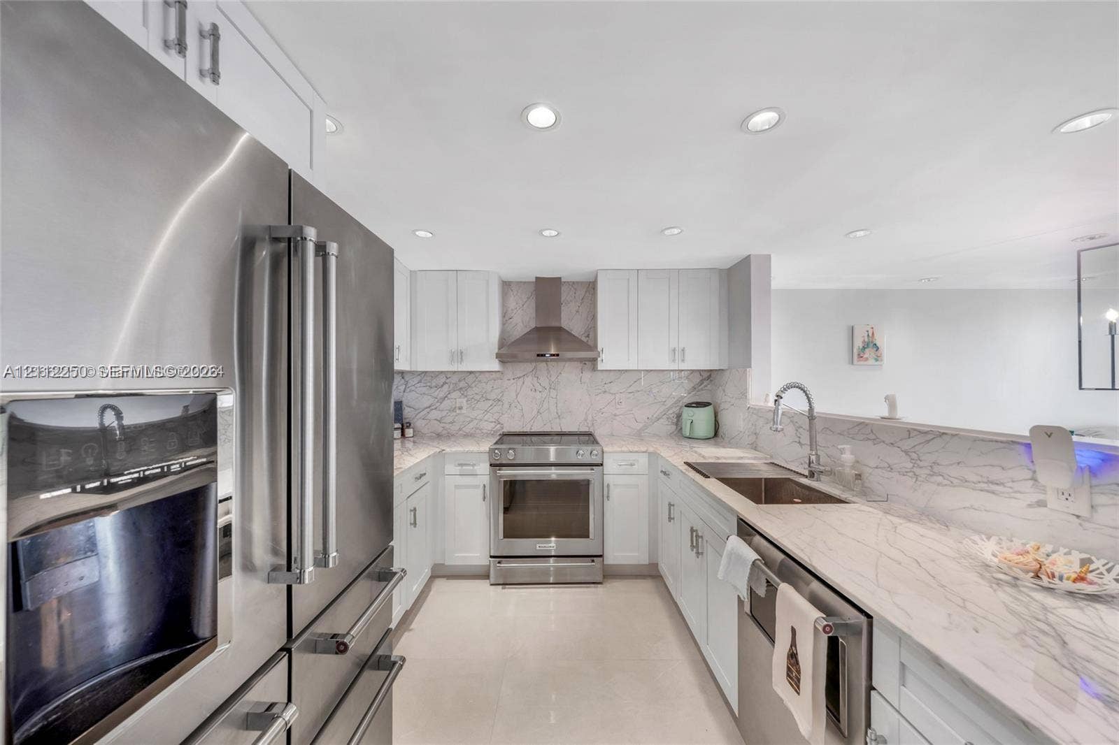 5838 Collins Avenue, #2F, Miami Beach, FL 33140 Kitchen featuring white cabinetry, stone-patterned backsplash, stainless steel appliances, and stone-patterned countertops with an integrated sink and gooseneck faucet