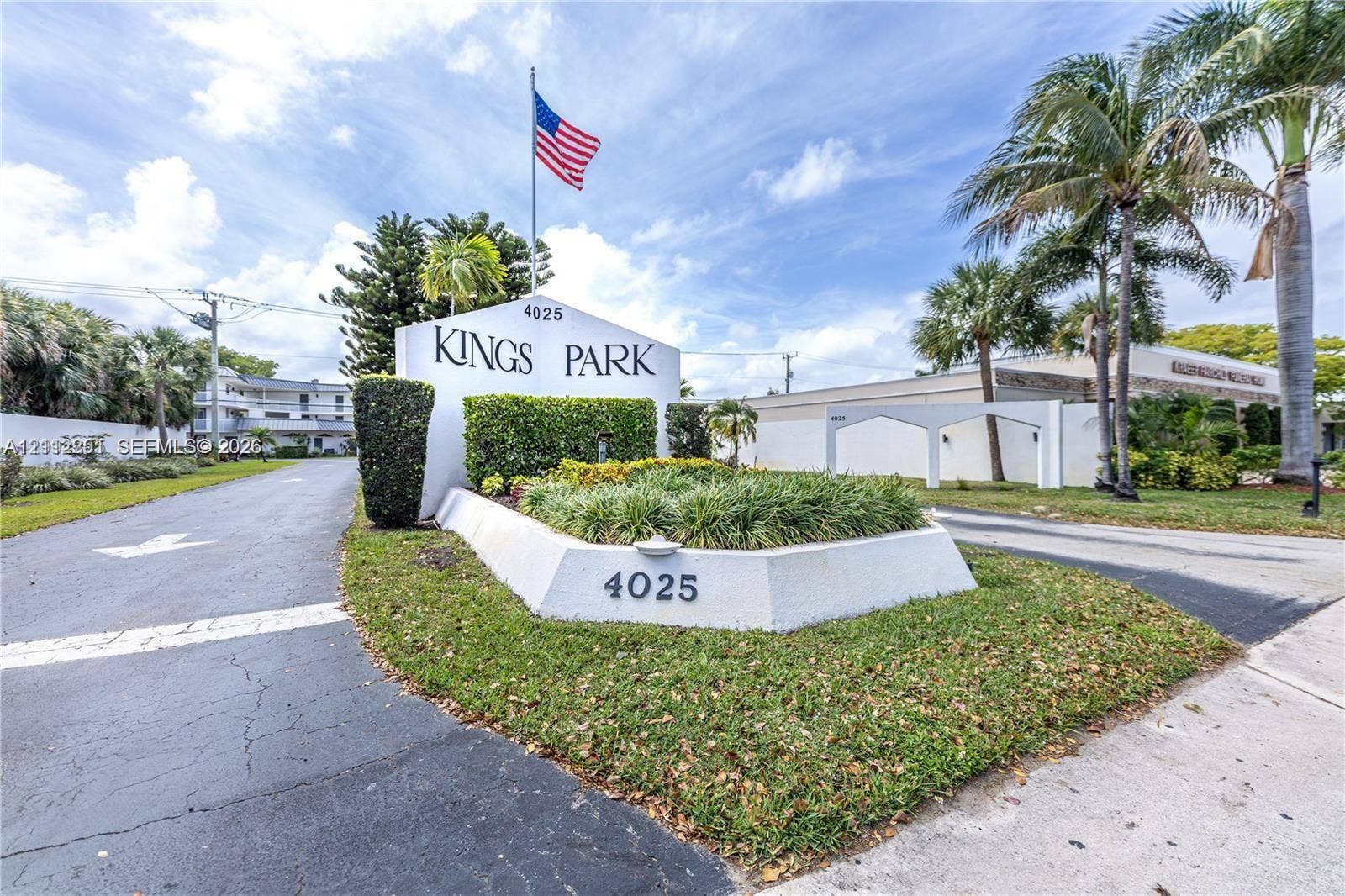 4025 N Federal Highway, #226C, Oakland Park, FL 33308 Kings Park entrance featuring a stucco monument sign, manicured landscaping, asphalt driveway, and mature palm trees