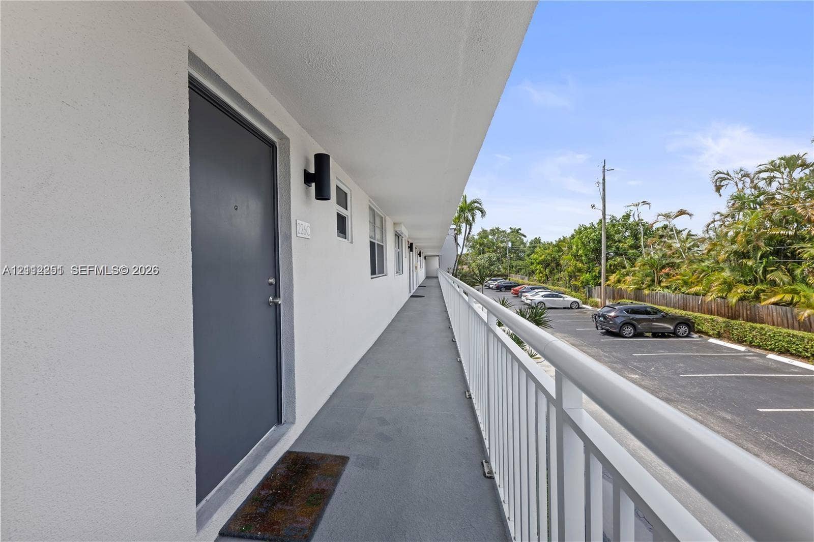 4025 N Federal Highway, #226C, Oakland Park, FL 33308 Exterior walkway featuring a painted solid-core door, cylindrical wall-mounted sconce lighting, and a white metal safety railing