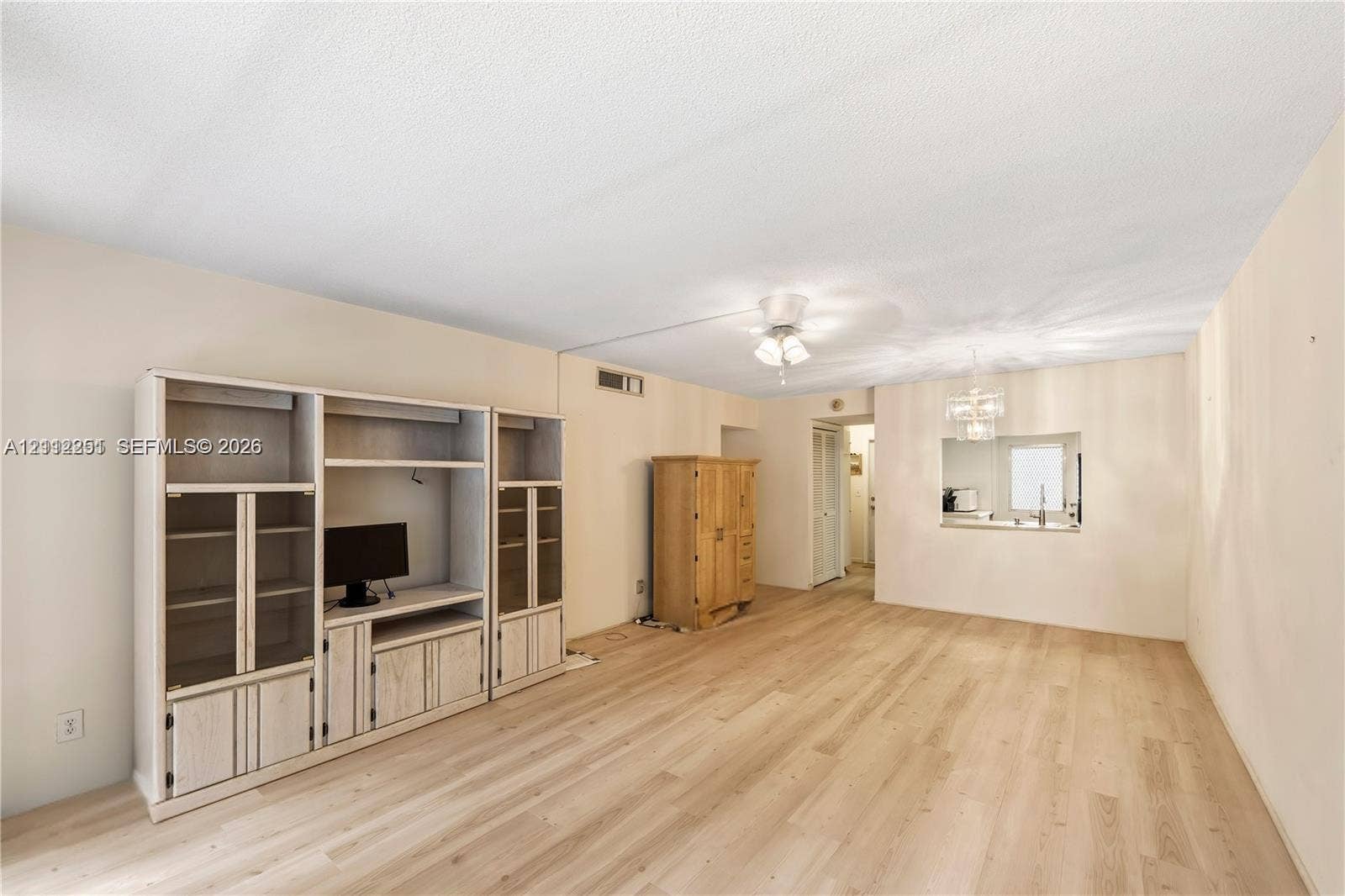 4025 N Federal Highway, #226C, Oakland Park, FL 33308 Living area featuring light-toned wood-finish flooring, built-in floor-to-ceiling cabinetry, recessed ceiling lighting, and a pass-through window to the kitchen